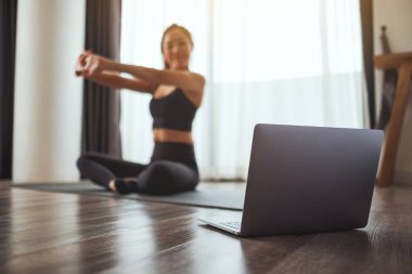 A beautiful young asian woman stretching arms while watching online workout tutorials on laptop at home
