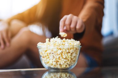 Close up image of a woman grabbing and picking pop corn from a bowl to eat while sitting on sofa at home
