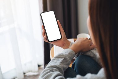 Üst görünümde, evde yatak odasında otururken elinde boş masaüstü ekran olan cep telefonu tutan bir kadının görüntüsü