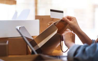 Çevrimiçi alışveriş için tablet bilgisayar ve kredi kartı kullanan genç bir kadının yakın plan fotoğrafı, masada alışveriş torbaları ve posta kutuları açılıyor