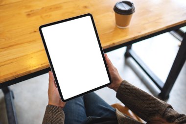 Siyah tabletli, beyaz ekranlı ve ahşap masada kahve fincanı olan bir kadının görüntüsü.