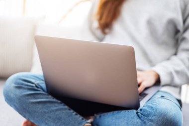 A beautiful woman using and working on laptop computer while sitting on a sofa at home