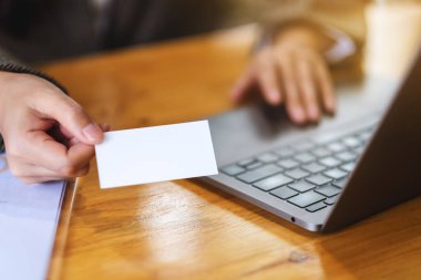 Ofiste dizüstü bilgisayar kullanırken elinde boş kartvizit tutan bir iş kadını.