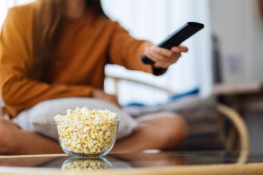 Patlamış mısır yiyen ve uzaktan kumandayla televizyon izlemek için kanalı arayan bir kadının görüntüsünü kapat.