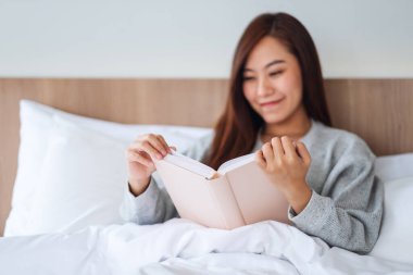 Evdeki rahat bir yatakta kitap okuyan güzel bir genç kadının yakın çekimi.