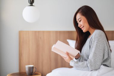 Evdeki rahat bir yatakta kitap okuyan Asyalı güzel bir kadının yakın plan görüntüsü.