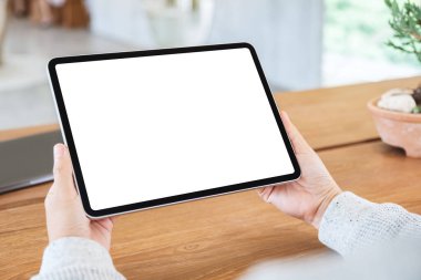 Ahşap masada beyaz ekranlı siyah tabletli bir kadının görüntüsü.