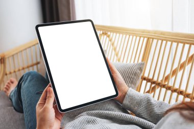 Evdeki kanepede yatarken elinde boş masaüstü beyaz ekran tableti olan bir kadının görüntüsü.