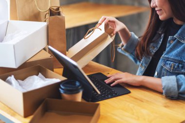 İnternetten alışveriş için tablet kullanan, alışveriş torbalarını açan ve posta kutusunu açan genç bir kadının yakın plan fotoğrafı.