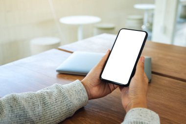 Boş beyaz masaüstü ekran ve ahşap masada dizüstü bilgisayarı olan cep telefonu tutan bir kadının görüntüsü. 