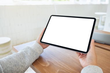 Ahşap masada beyaz ekranlı siyah tabletli bir kadının görüntüsü.