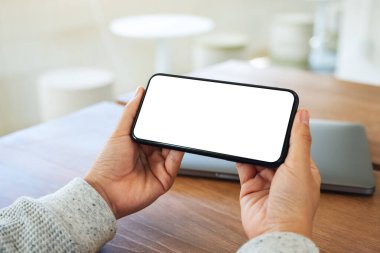 Boş beyaz masaüstü ekran ve ahşap masada dizüstü bilgisayarı olan cep telefonu tutan bir kadının görüntüsü. 