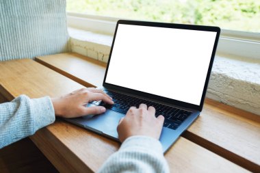 Laptop bilgisayar klavyesinde yazı yazan ve kullanan bir kadının resmi. Tahta masadaki boş beyaz masaüstü ekran.
