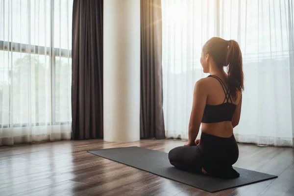 stock image Rear view image of a beautiful young asian woman sitting on training mat preparing to workout at home