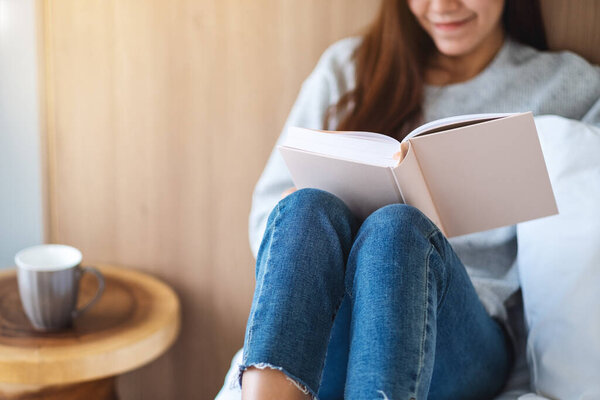 Крупный план красивой молодой женщины, читающей книгу в белой уютной кровати дома