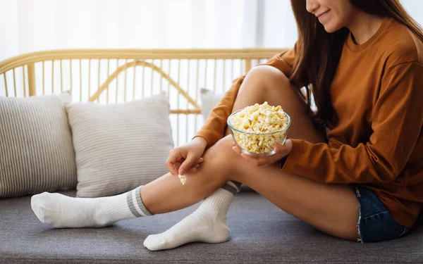 一个漂亮的年轻女子坐在沙发上拿着和吃着爆米花的近照 — 图库照片