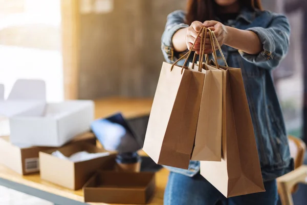 网上购物时 一名妇女拿着购物袋 桌上放着平板电脑和邮筒 展示购物袋的造型 — 图库照片