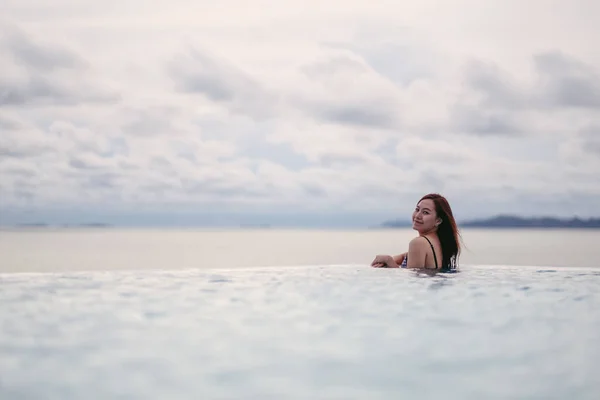 一个年轻的亚洲女人在无限大的游泳池里放松 看着美丽的海景 — 图库照片