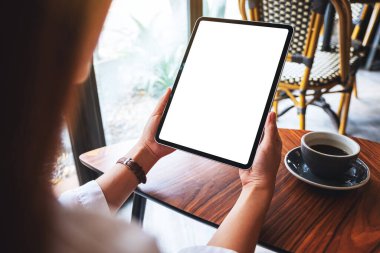 Masasında kahve fincanı olan siyah tabletli beyaz ekranlı bir kadının görüntüsü.