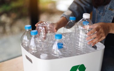 Geri dönüşümlü çöp şişelerini toplayıp evdeki çöp kutusuna koyan bir kadın.