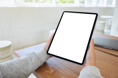 Ahşap masada beyaz ekranlı siyah tabletli bir kadının görüntüsü.