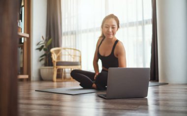 A beautiful young asian woman watching online workout tutorials on laptop at home