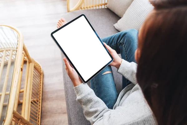 Üst görünümde, evde bir kanepede yatarken elinde boş masaüstü beyaz ekranı olan siyah tablet bir kadının görüntüsü var.