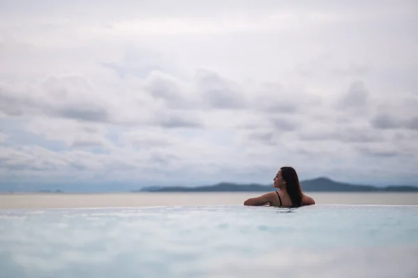 一个年轻的亚洲女人在无限大的游泳池里放松 看着美丽的海景 图库图片