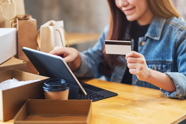 一位年轻女性在网上购物时使用平板电脑和信用卡 桌上有邮筒和购物袋的照片 图库照片