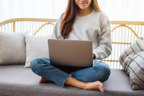 一位年轻女性坐在沙发上使用和使用笔记本电脑的图片 免版税图库照片