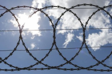 Yine dikenli teller mavi bulutlu gökyüzü. Hapishane kavramı.