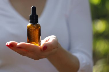 Ellerinde kozmetik şişesi, bulanık kadın silueti. Amber kozmetik el düşürme şişesi..