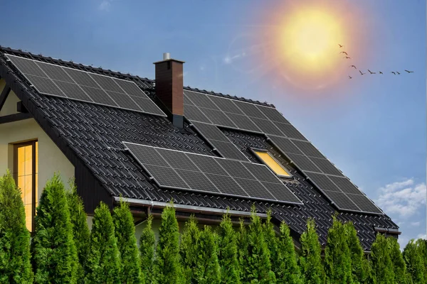 Modern house with black solar panels on roof. Photovoltaic panels on roof. Light in windows, green energy concept.