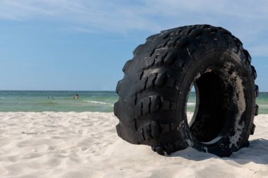 A large tyre over the coast, the beach. Eco problems, ocean pollution