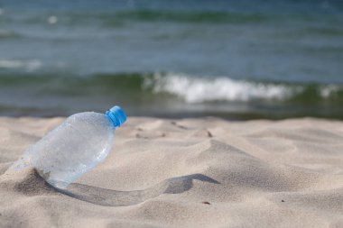 Plastic drink bottle washed up at beach. Close-up, selective focus, transparent PET.
