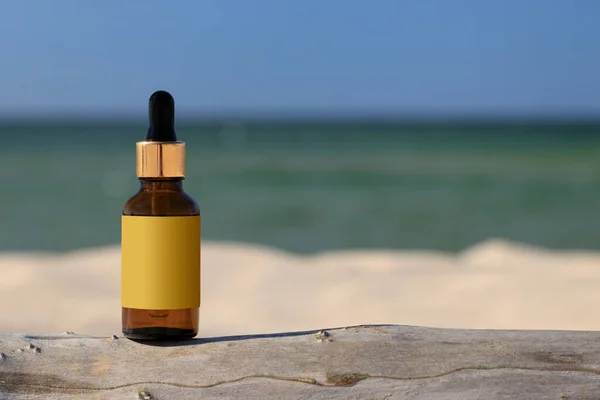 A dropper amber bottle against the backdrop of a blurred beach. Summer light, positive atmasphere. Mock-up for a cosmetic product. Empty label