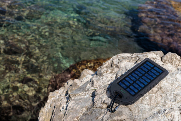 Battery solar energy device against the background of a beautiful beach. Charging your smartphone from the solar battery.