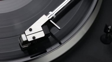 Siyah bir vinil plaka üzerinde giden bir pikabın üst görüntüsü. Eski gramofon vinil disk çalıyor, yakın plan..