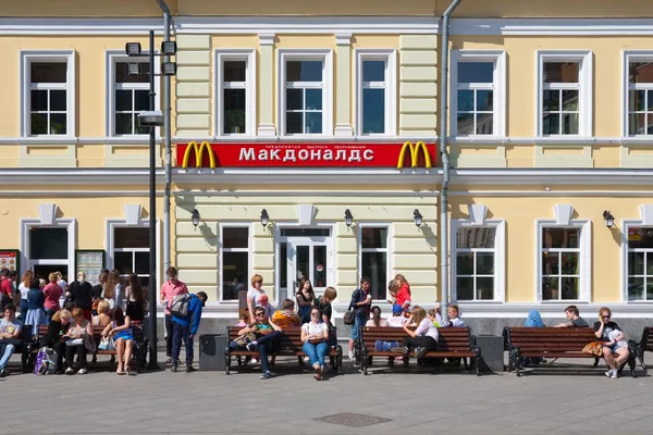 Personas descansando en bancos cerca del edificio del restaurante McDonald 's — Foto de Stock