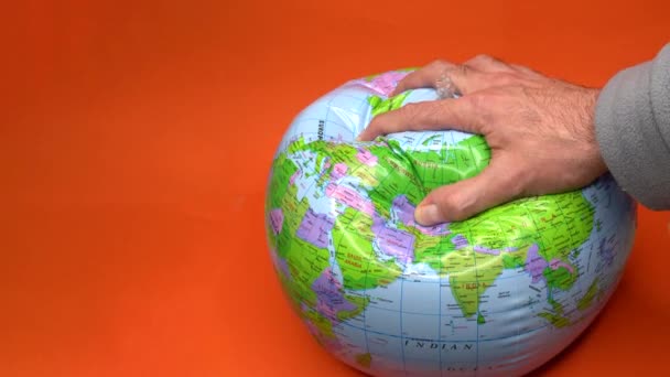 Hand deflating a world globe on orange background. — Stock Video