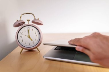 Clock marking 5 pm and a laptop with the lid closed. Concepts such as quiet quitting, coffee break or taking a break at work