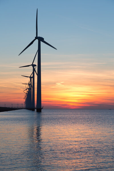 Длинный ряд ветряных турбин с закатом над морем
