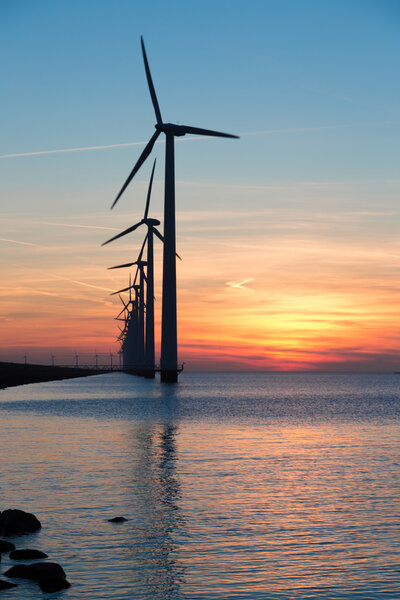 Длинный ряд ветряных турбин с закатом над морем
