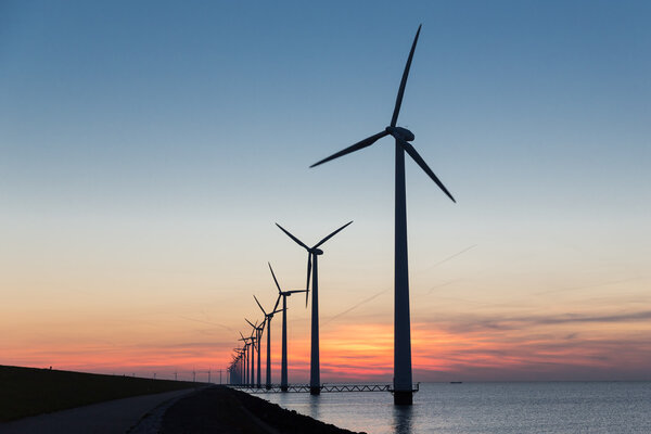 Голландский ряд оффшорных ветряных турбин на красивом закате
