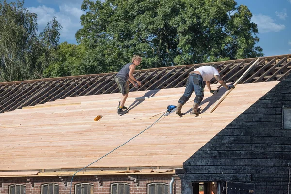 Двое строителей заняты ремонтом крыши деревянного сарая — стоковое фото