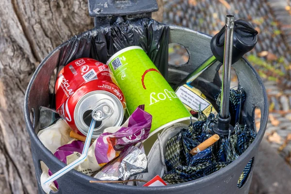 Lixeira com lixo, guarda-chuva partido, latas de refrigerante e pontas de cigarro — Fotografia de Stock