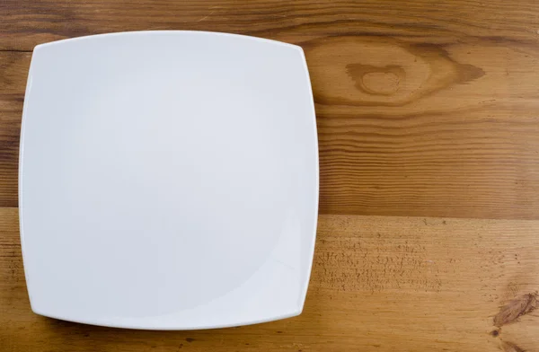 Белая тарелка на коричневом столе — стоковое фото