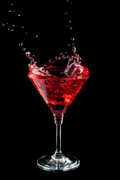 Red cocktail splashing into glass on black — Stock Photo, Image