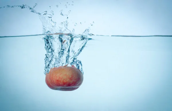 Peach drop in blue water with splashes — Stock Photo, Image
