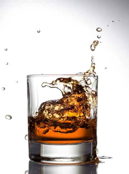 Whisky schizzare fuori dal vetro su un bianco — Foto Stock